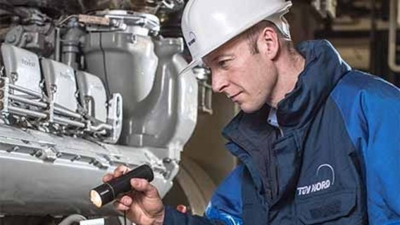 Blockheizkraftwerke Das Bild zeigt einen TÜV-Mitarbeiter, der mit einer Taschenlampe ein Bauteil eines BHKW begutachtet.