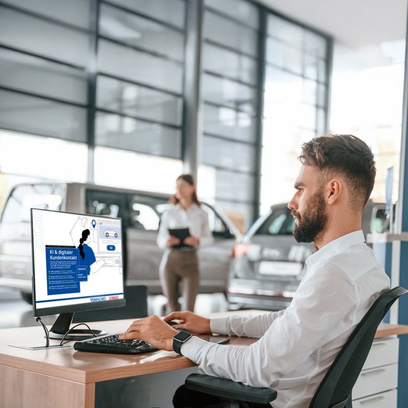 Digitaler Kundenservice im Autohaus, TÜV NORD INSIGHT Mitarbeiter am Computer in einem Autohaus, Bildschirm zeigt Informationen über digitalen Kundenkontakt. Autos und Person mit Tablet im Hintergrund.