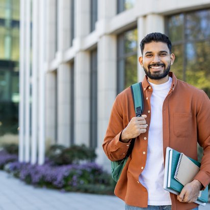 A smiling male student stands in front of a building.