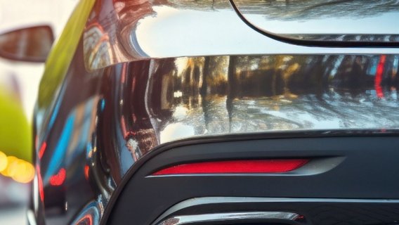 Detailaufnahme des Hecks eines glänzenden schwarzen Sportwagens mit leuchtenden roten LED-Rücklichtern. Im Hintergrund ist eine unscharfe Stadtstraße mit Bäumen und Bokeh-Lichteffekten zu sehen.