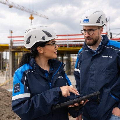 Baubegleitendes-Qualitätscontrolling Zwei TÜV NORD-Mitarbeitende mit Helmen und Tablets im Gespräch auf einer Baustelle beim baubegleitenden Qualitätscontrolling