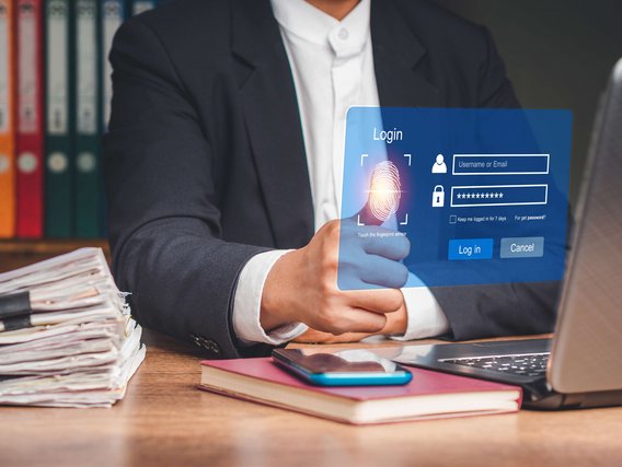 Person im Anzug nutzt Fingerabdrucksensor auf einem holografischen Login-Interface vor einem Laptop.