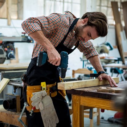 Präzises Arbeiten in der Holzwerkstatt mit Bohrmaschine. Handwerker bohrt konzentriert in ein Holzstück in einer Werkstatt.