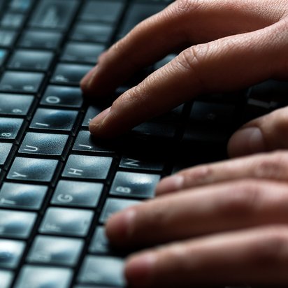 Zwei Hände tippen auf PC-Tastatur. Großaufnahme zweier Hände, die auf einer schwarzen PC-Tastatur tippen.