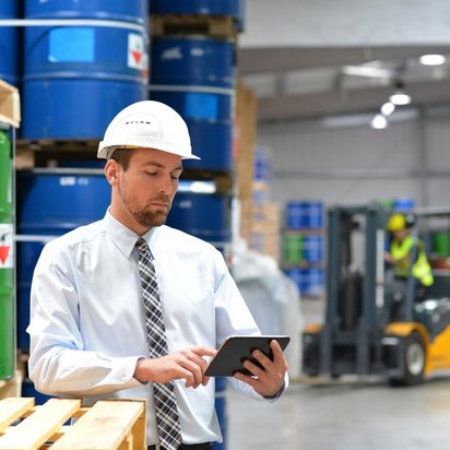 Beauftragter neben Gefahrgut Ein Beauftragter in Sicherheitskleidung steht mit Tablet in den Händen neben Gefahrgut in Fässern.