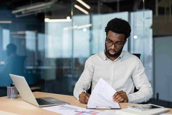 Person arbeitet an einem Schreibtisch mit Laptop und Dokumenten in einem modernen Büro.