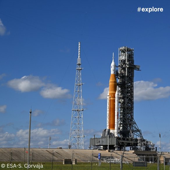 Rakete auf der Startrampe Eine große Rakete steht auf einer Startrampe, umgeben von hohen Türmen und technischen Anlagen. Der Himmel ist klar und blau mit einigen Wolken. Die Szene vermittelt den Eindruck von technologischem Fortschritt und Raumfahrt.