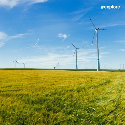 Windkraftanlagen in der Landschaft Eine Reihe von Windkraftanlagen steht in einem weiten Feld mit grünem Gras unter einem klaren blauen Himmel. Der Hashtag "#explore" ist oben rechts im Bild zu sehen.