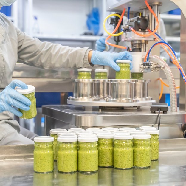 Verpackung von Lebensmitteln an einer Abfüllanlage Mitarbeiter befüllt Gläser an einer Abfüllanlage mit einem grünen, cremigen Lebensmittel