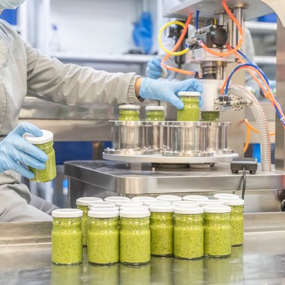 Verpackung von Lebensmitteln an einer Abfüllanlage Mitarbeiter befüllt Gläser an einer Abfüllanlage mit einem grünen, cremigen Lebensmittel