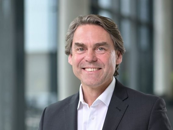 Porträtaufnahme von Jacques Kruse Brandao in dunklem Anzug mit weißem Hemd vor einem hellen, professionellen Büroumgebung.