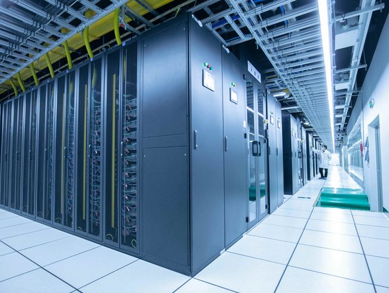 Blick in einen modernen Serverraum mit langen Reihen von Server-Racks und einem Techniker, der die Systeme überprüft.