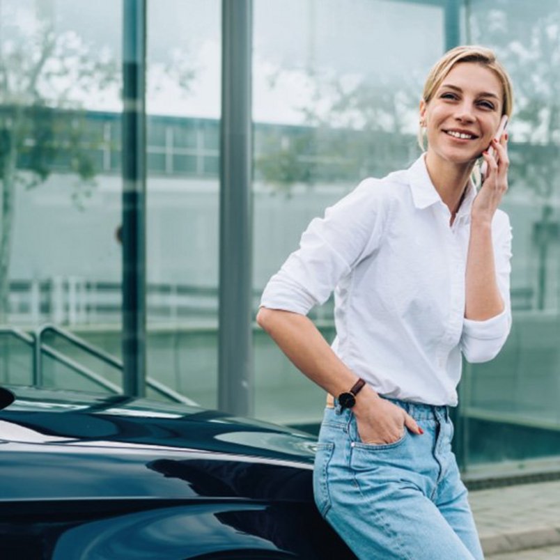 Telefonat am Auto vor modernem Gebäude Frau lehnt sich an Auto und telefoniert