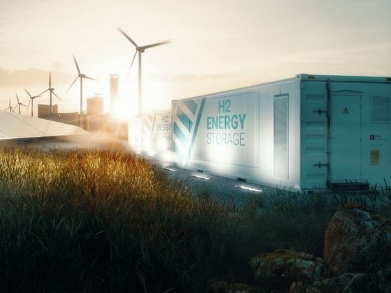 Hydrogen storage A hydrogen energy storage container marked 'H2 ENERGY STORAGE' in turquoise color, set against a sunset background with wind turbines and industrial buildings. Ground lighting illuminates the container while tall grass grows in the foreground.