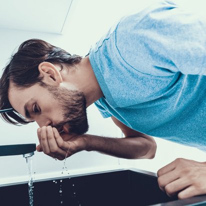 Person beugt sich über ein Waschbecken und schöpft Wasser aus einem Wasserhahn.