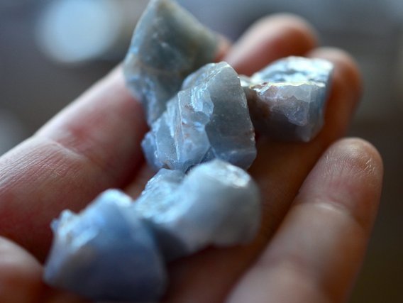 A hand is holding raw, natural, chunky blue calcite minerals A hand is holding raw, natural, chunky blue calcite minerals