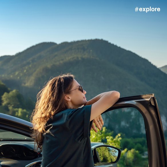 Entspannung in der Natur Eine Person lehnt sich entspannt an die geöffnete Autotür und blickt auf eine malerische Berglandschaft. Die Sonne scheint hell und die grünen Hügel erstrecken sich bis zum Horizont.