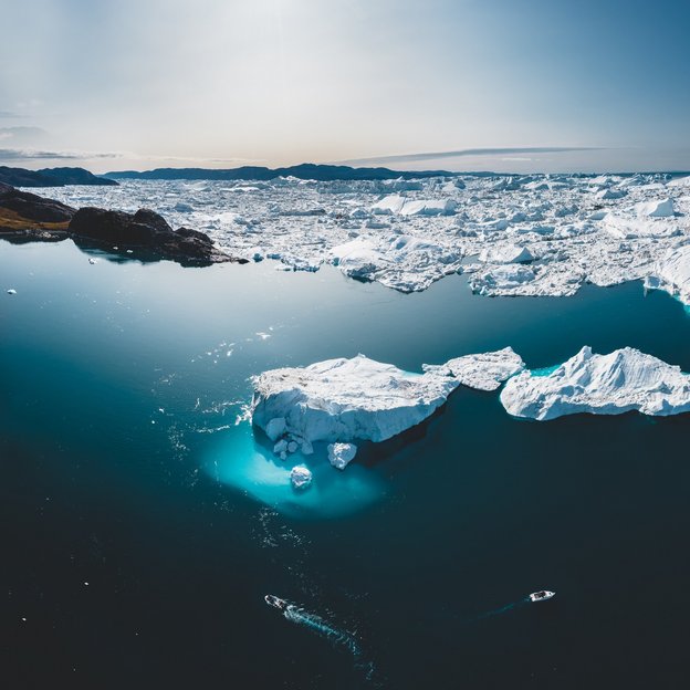 Schmelzende Eisberge in der Arktis als Folge des Klimawandels Luftaufnahme von schmelzenden Eisbergen in der Arktis mit zwei Booten im Wasser