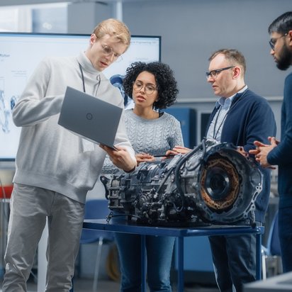 Gruppe von Ingenieuren diskutiert über ein Automobilteil in einem technischen Labor.