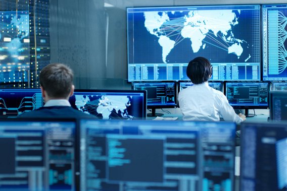 IT-Spezialisten überwachen globale Netzwerksysteme in einem Kontrollzentrum mit mehreren Bildschirmen.