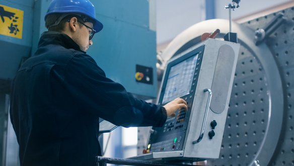 Moderne Fertigungstechnik in der industriellen Produktion Techniker mit Schutzhelm bedient eine moderne CNC-Maschine in einer Produktionshalle