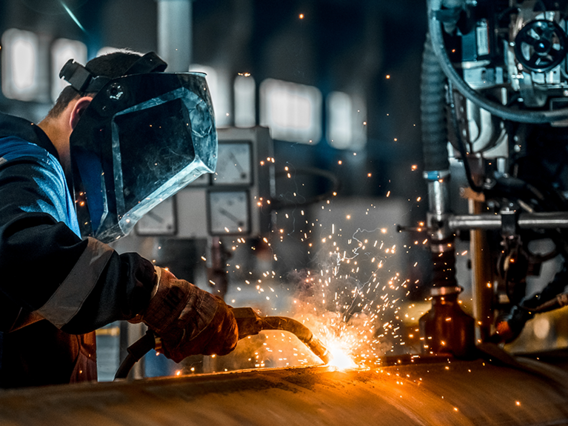 Strompreiskompensation (SPK) – Unterstützung für energieintensive Unternehmen mit ISO 50001 Industriearbeiter mit Schweißgerät bei der Metallbearbeitung – energieintensive Produktion mit hohem Stromverbrauch