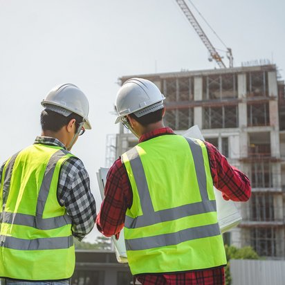 SCC - Personal SCC - Personal: Zwei Personen des Baugewerbes befinden sich auf einer Baustelle. Beide männlichen Personen tragen Schutzkleiden wie Westen und Helme.