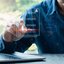 Person interagiert mit einem digitalen Dokument auf einem Laptop, während sie ein Smartphone hält.