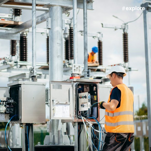 Wartungsarbeiten an elektrischer Industrieanlage Technische Fachkraft arbeitet an einem geöffneten Schaltschrank in einer elektrischen Industrieanlage mit Schalt- und Verteilungstechnik im Außenbereich.