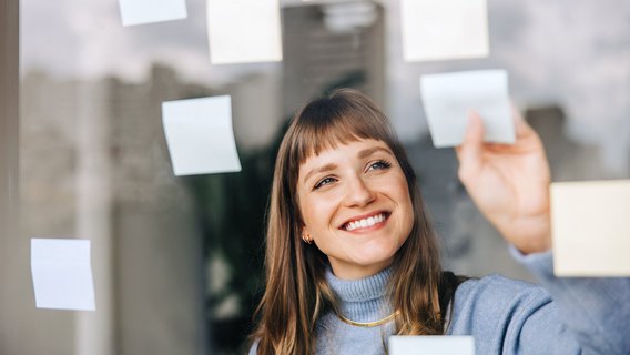 TÜV NORD Personenzertifizierungen Eine junge Frau klebt Post-its an eine Scheibe