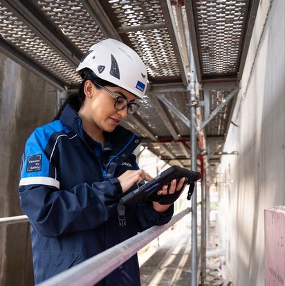 Prüfung-Baumängel TÜV NORD-Mitarbeiterin mit Helm prüft bauliche Details auf einer Baustelle und dokumentiert mögliche Baumängel.