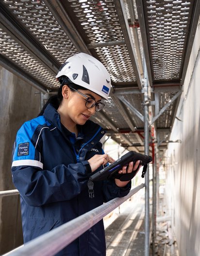 Prüfung-Baumängel TÜV NORD-Mitarbeiterin mit Helm prüft bauliche Details auf einer Baustelle und dokumentiert mögliche Baumängel.