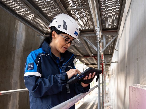 Prüfung-Baumängel TÜV NORD-Mitarbeiterin mit Helm prüft bauliche Details auf einer Baustelle und dokumentiert mögliche Baumängel.