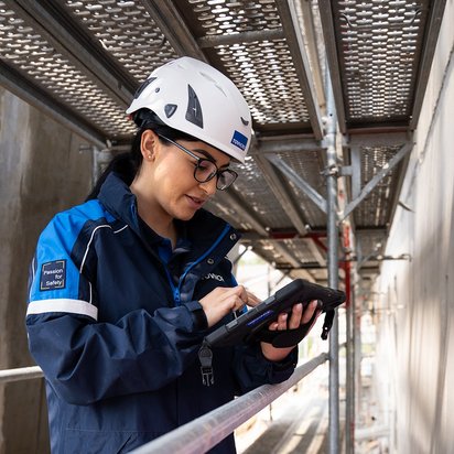 Prüfung-Baumängel TÜV NORD-Mitarbeiterin mit Helm prüft bauliche Details auf einer Baustelle und dokumentiert mögliche Baumängel.