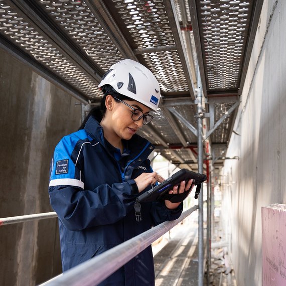 Prüfung-Baumängel TÜV NORD-Mitarbeiterin mit Helm prüft bauliche Details auf einer Baustelle und dokumentiert mögliche Baumängel.