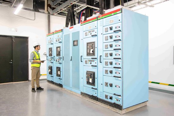 Techniker im Sicherheitshelm und Warnweste überprüft elektrische Schalttafeln in einem Kontrollraum.