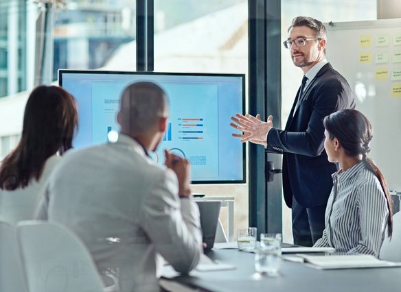 Professionelle Geschäftspräsentation mit Datenanalyse im Teammeeting. Geschäftsmann präsentiert vor Kollegen Diagramme auf einem großen Bildschirm im Konferenzraum.