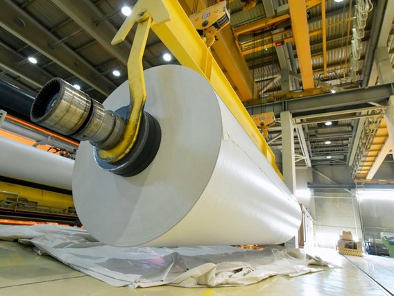 Paper production in a factory – a large paper roll is being moved by a crane Paper production in a factory – a large paper roll is being moved by a crane