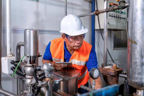 Industrielle Anlagenprüfung durch erfahrenen Techniker Techniker mit Schutzhelm und Warnweste inspiziert industrielle Rohrleitungen und Anlagenkomponenten