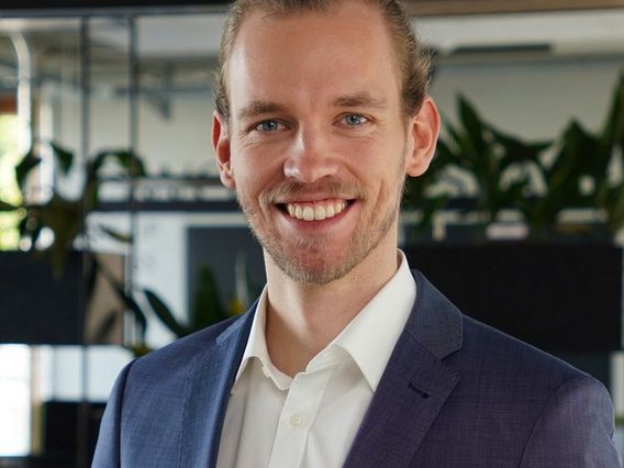 Patrick Krieger A professional portrait of Patrick Krieger in a navy blue suit, standing in a modern office.
