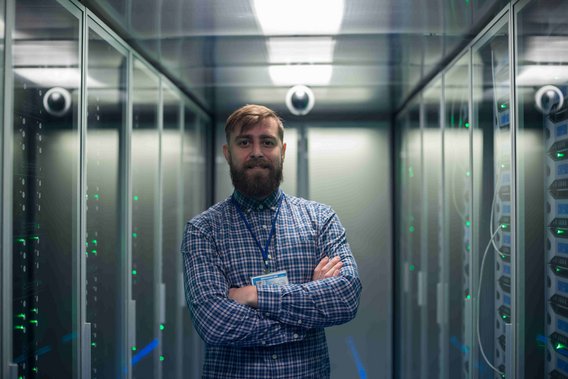 Person steht mit verschränkten Armen in einem Serverraum zwischen zwei Reihen von Server-Racks.