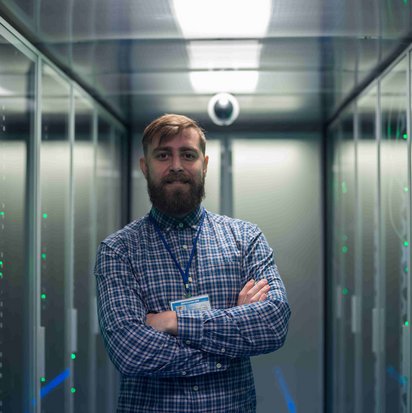 Person steht mit verschränkten Armen in einem Serverraum zwischen zwei Reihen von Server-Racks.