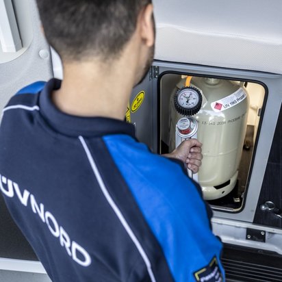 Gasanlagenprüfung Wohnwagen Ein Mann mit einem TÜV NORD T-shirt prüft die Gasanlage in einem Wohnmobil