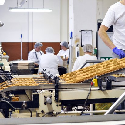 Lebensmittelsicherheit in der industriellen Lebensmittelproduktion Mitarbeitende an einem Laufband der Keksherstellung in weißen Shirts und mit Hauben