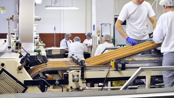 FSSC 22000 Version 7 für die lebensmittelherstellende Industrie Mitarbeitende an einem Laufband der Keksherstellung in weißen Shirts und mit Hauben