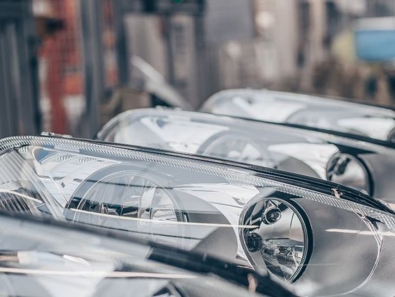 Nahaufnahme mehrerer Autoscheinwerfer in einer Reihe, die die moderne Fahrzeugbeleuchtungstechnologie zeigen, mit unscharfem industriellem Hintergrund.