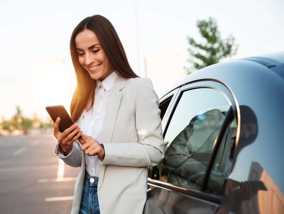 MPU preparation & Co. Woman standing next to a car with a smartphone in her hand.