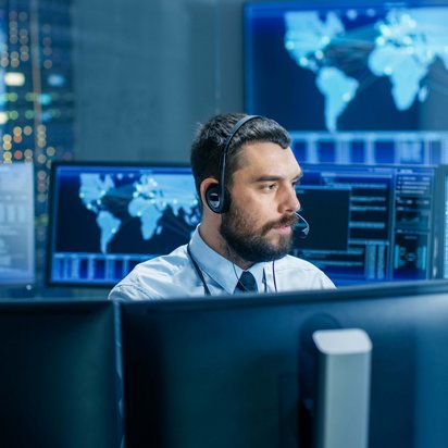 IT-Spezialist überwacht Netzwerksysteme in einem Kontrollzentrum mit mehreren Bildschirmen.