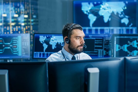 IT-Spezialist überwacht Netzwerksysteme in einem Kontrollzentrum mit mehreren Bildschirmen.