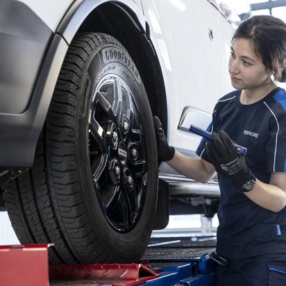 Schadengutachten TÜV NORD Auto auf Hebebühne und eine Frau steht mit einer Lampe am vorderen Reifen